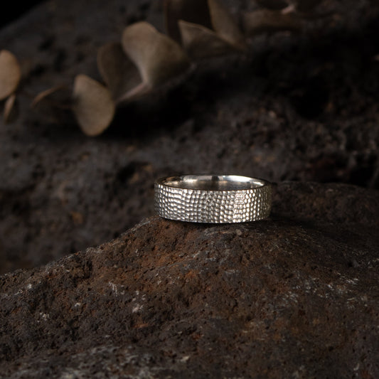 Handmade sterling silver wedding ring displayed on a textured stone background.