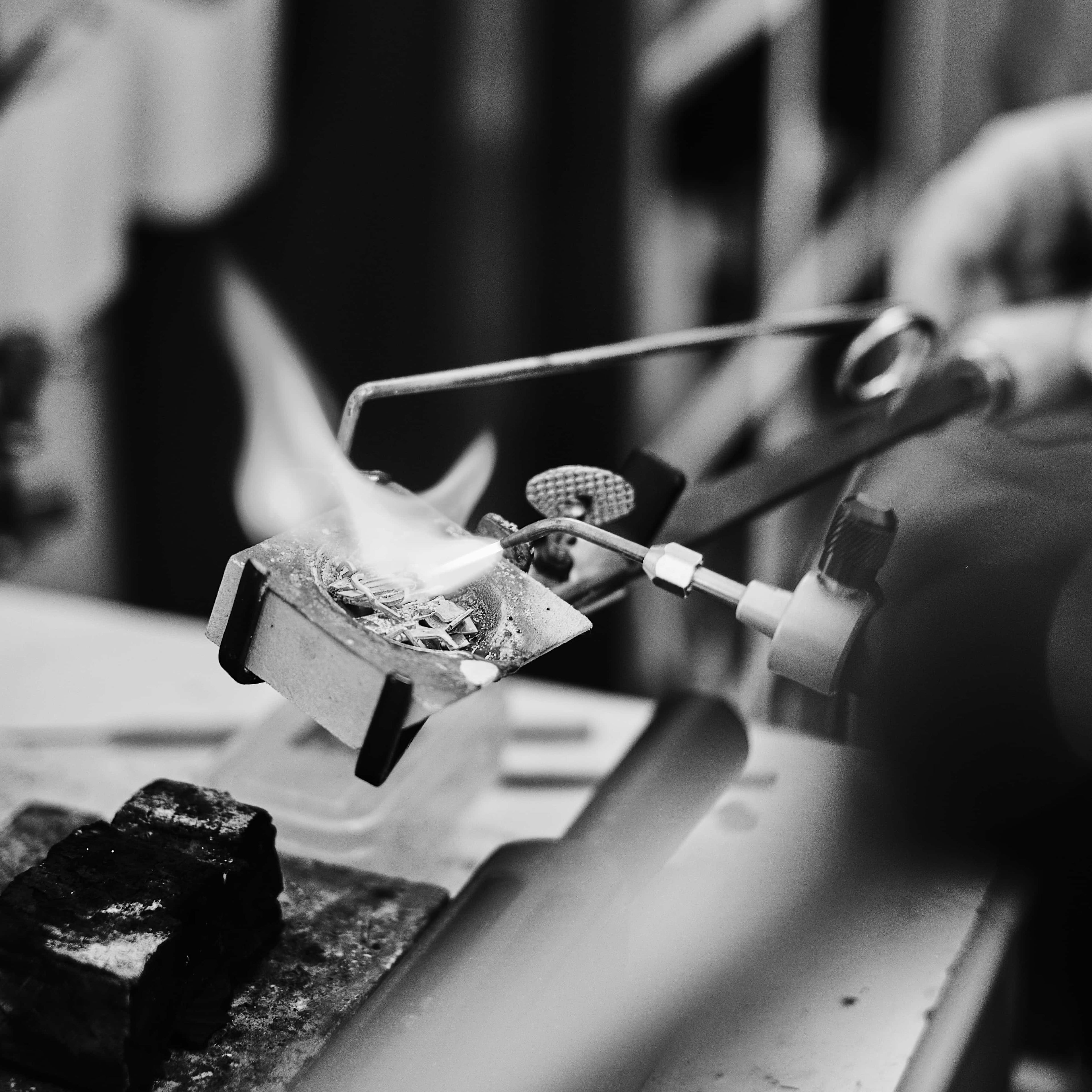 Silversmith soldering a silver piece with a torch flame in the studio.