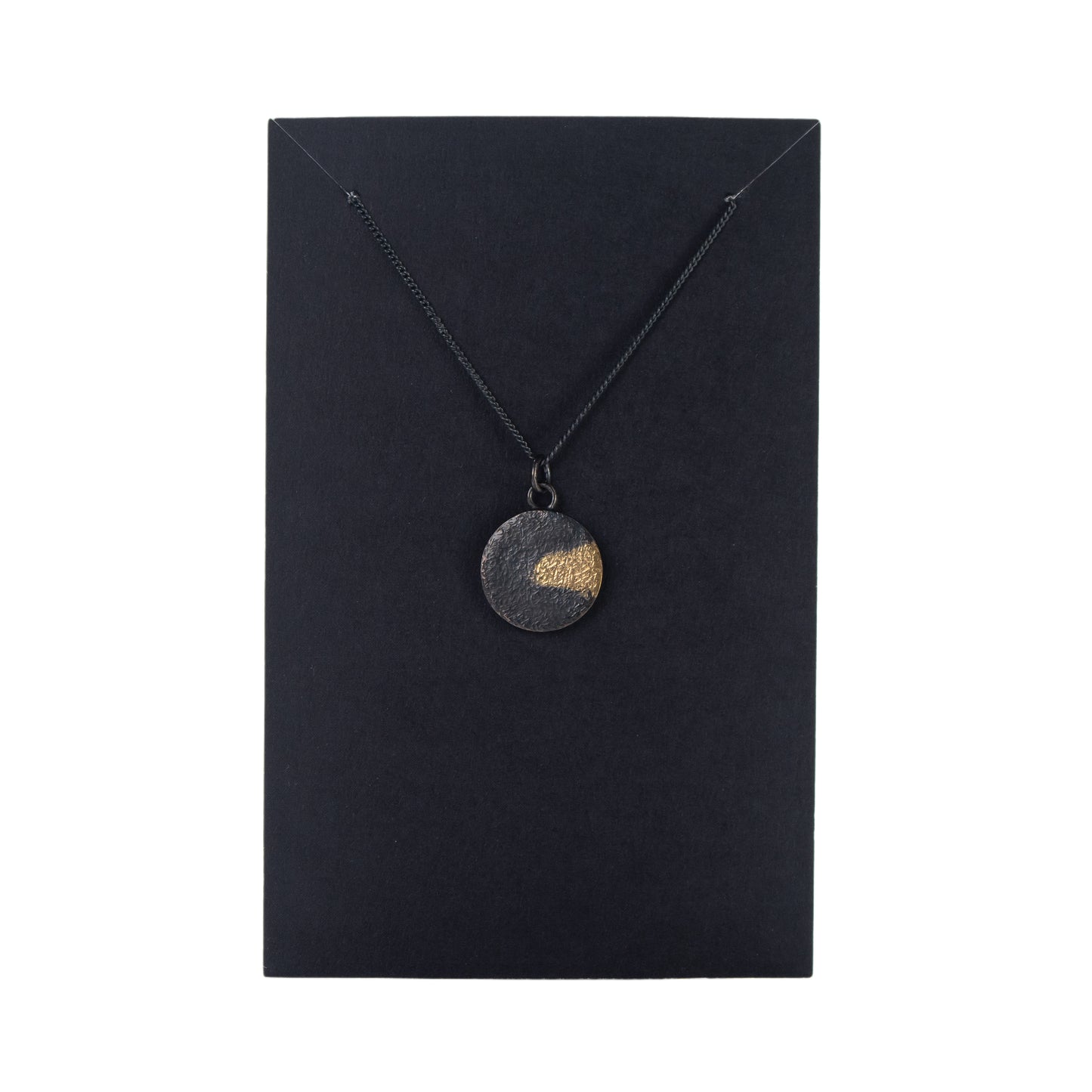 Oxidised silver disc pendant with gold detail displayed on black jewellery card