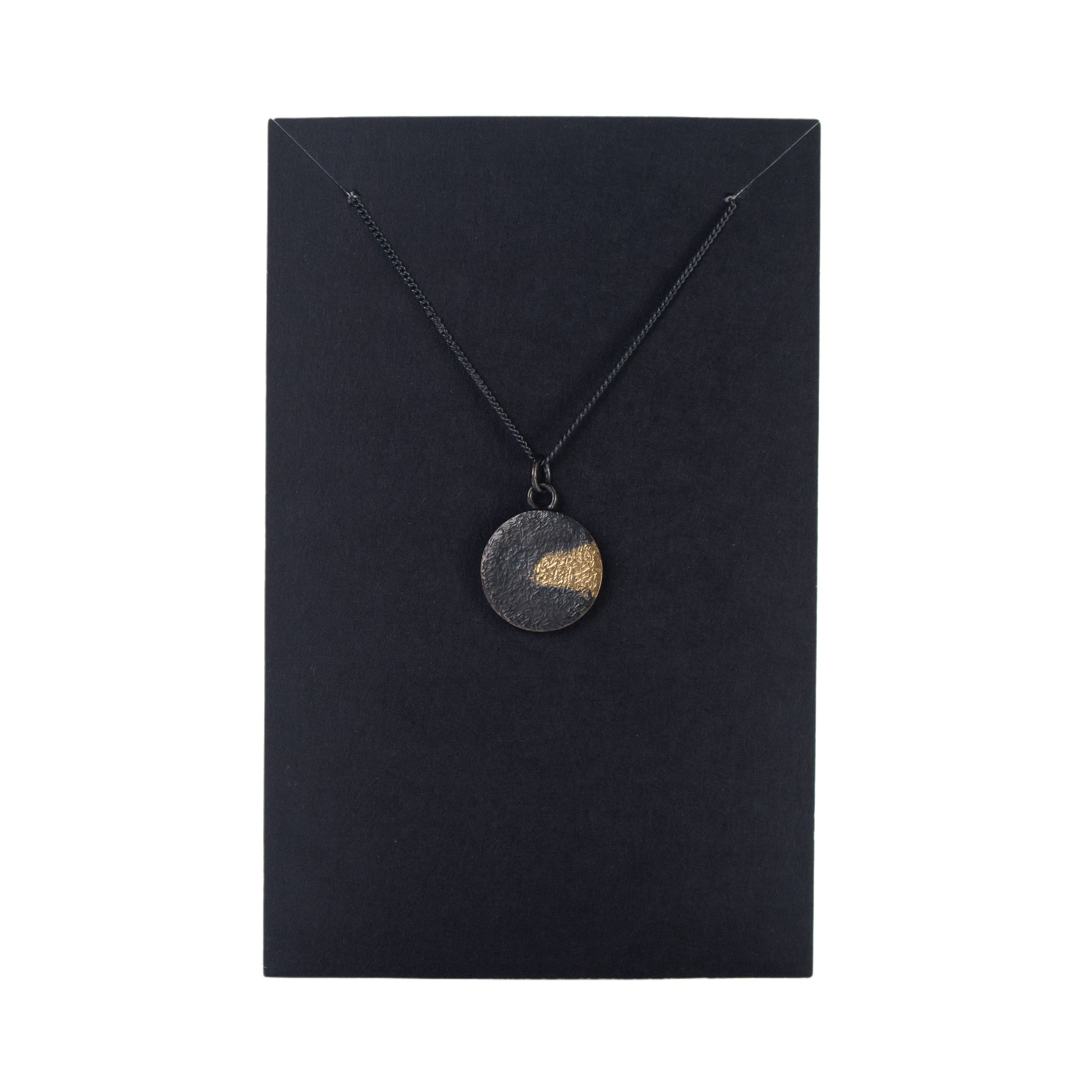Oxidised silver disc pendant with gold detail displayed on black jewellery card