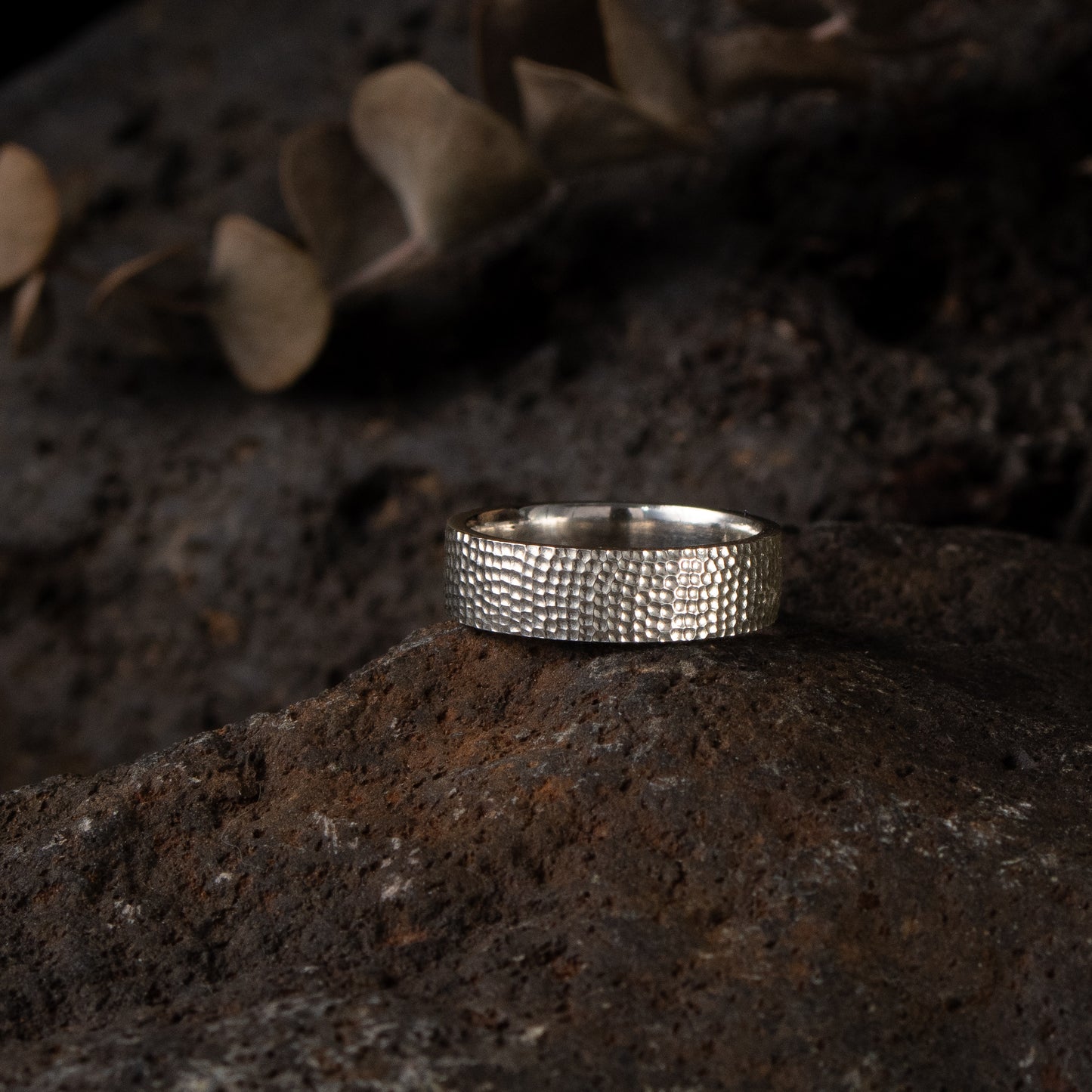 Textured silver band ring in sterling silver with a hand-carved surface on styled background